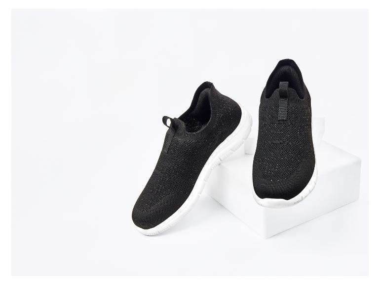 Une paire de baskets noires à enfiler avec des semelles blanches sur un piédestal blanc.
