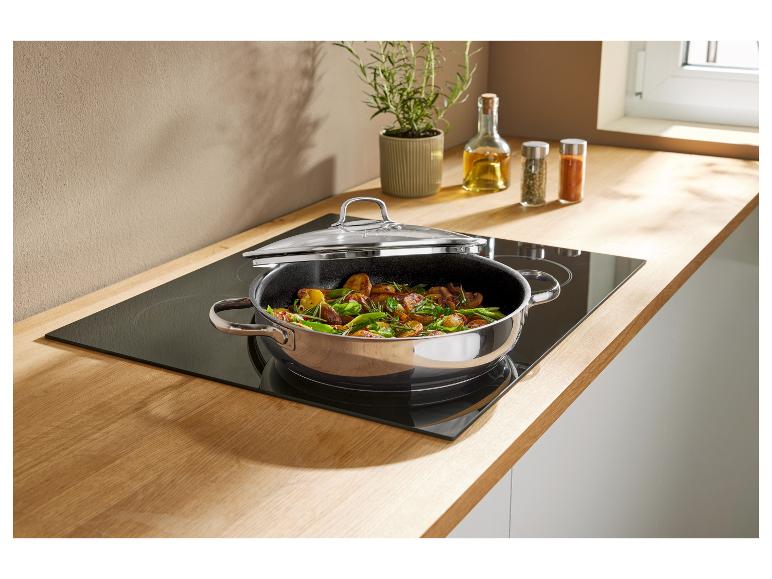 Poêle de légumes sur une plaque à induction, avec plantes et épices en arrière-plan.