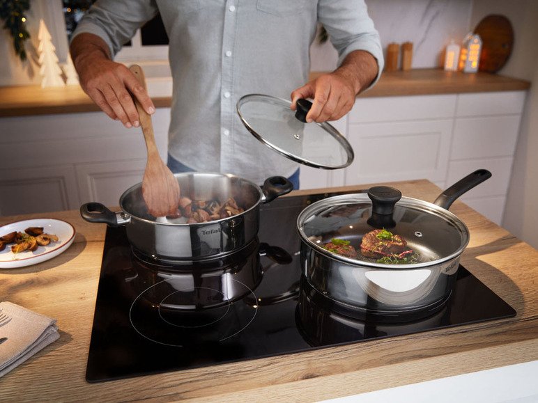 Un homme cuisine dans une casserole Tefal avec couvercle sur une plaque à induction.
