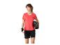 Femme en t-shirt de sport corail, short noir et gants de cyclisme, tenant un casque.