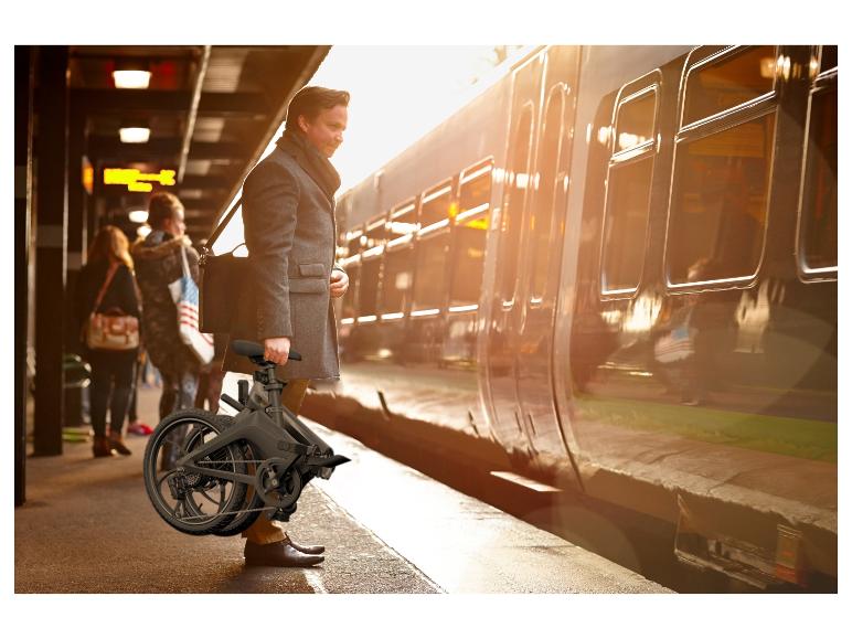 Homme en manteau tenant un vélo pliant sur un quai à côté d'un train.
