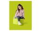 Fille souriante en haut rose et leggings gris, assise sur un pouf vert.