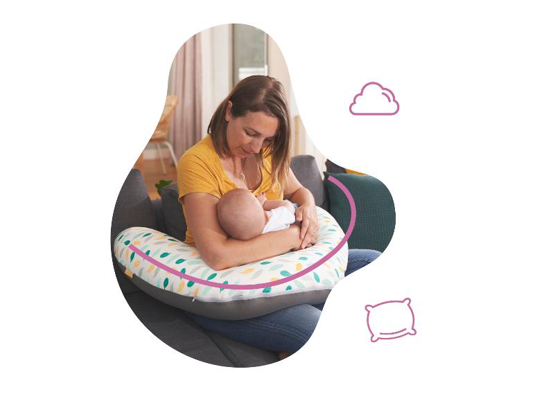 Une mère allaite son bébé confortablement installé sur un coussin d'allaitement.
