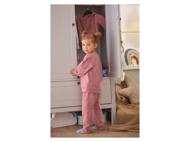Petite fille en survêtement rose ouvrant la porte d'une armoire.