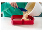 Une pâte à gâteau est versée dans un moule en silicone rouge.