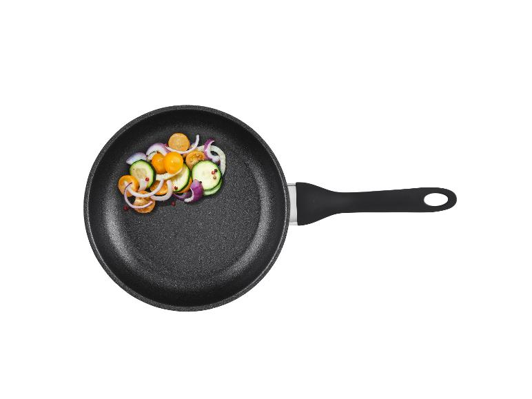 Une poêle noire avec des tomates, des courgettes et des oignons coupés.