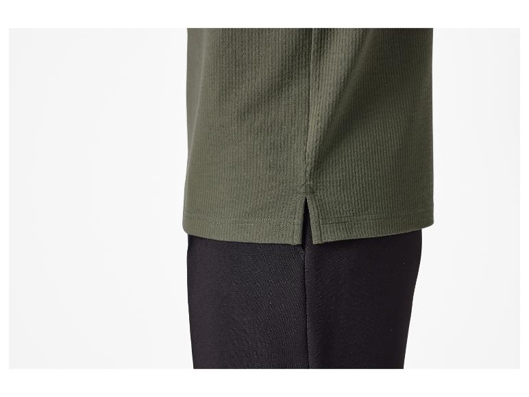Détail de l'ourlet inférieur d'un t-shirt vert avec fentes latérales.