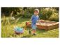 Enfant heureux tirant une charrette de jouets avec des jouets de sable à côté d'un bac à sable dans un jardin.