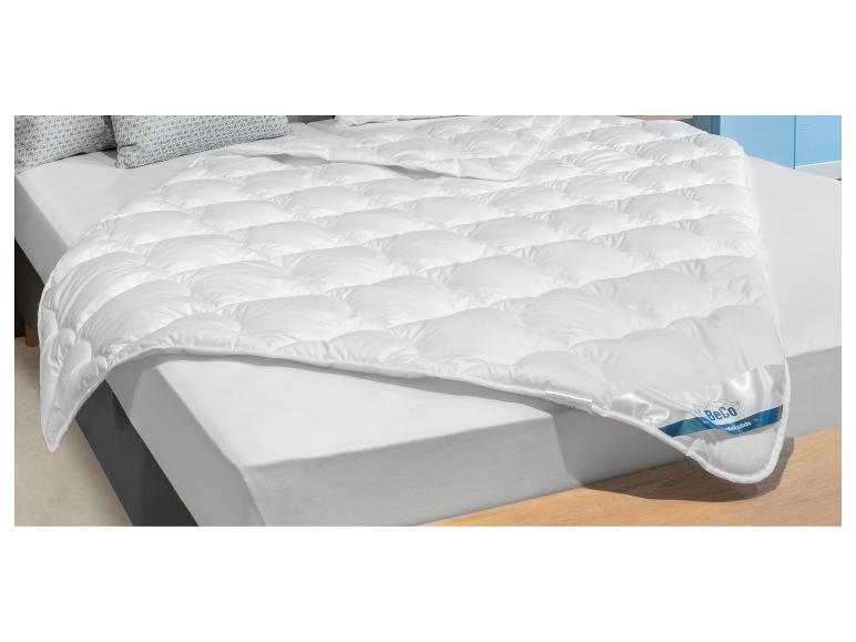 Couette blanche matelassée BeCo sur un lit avec oreillers à motifs.