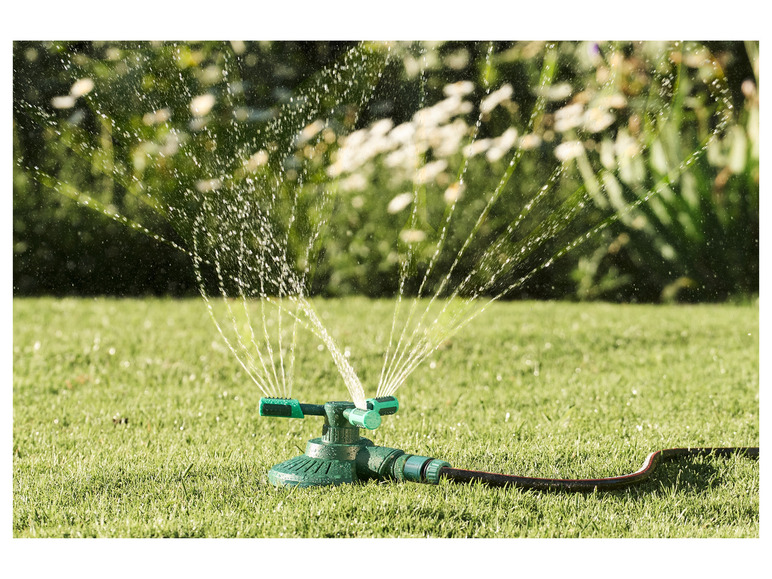 Un arroseur vert avec un tuyau arrosant une pelouse.