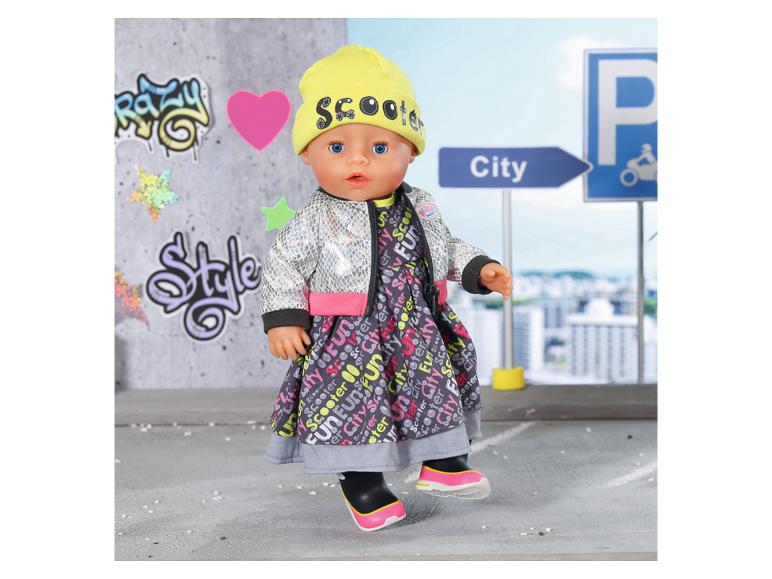 Poupée en robe imprimée ville, veste argentée et bonnet jaune avec le mot 'Scooter'.