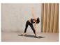 Une femme en vêtements de sport noirs fait du yoga sur un tapis.