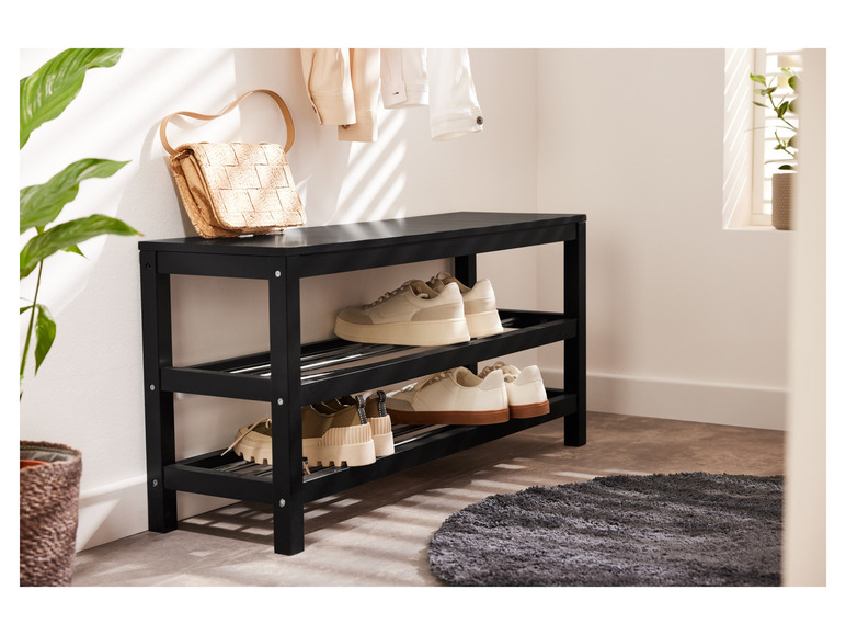 Une étagère à chaussures noire avec des baskets blanches et un sac en paille.