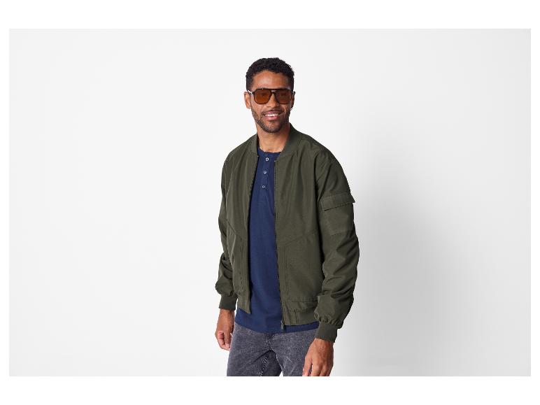 Homme en blouson aviateur vert foncé, chemise henley bleu marine et jean foncé
