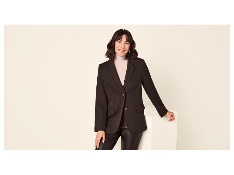 Femme en blazer noir et pantalon en cuir souriant à la caméra.
