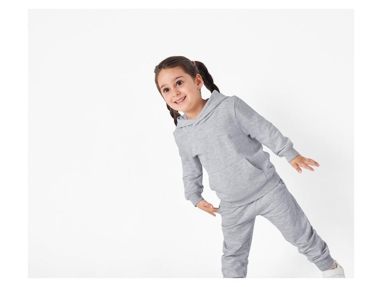 Une jeune fille portant un sweat-shirt à capuche gris et un pantalon de survêtement.