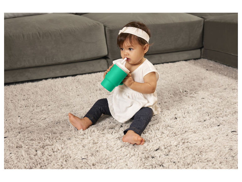 Bébé boit avec un gobelet à paille sur un tapis.