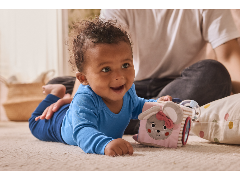Bébé heureux en grenouillère bleue jouant avec un cube d'activités doux sur le tapis.