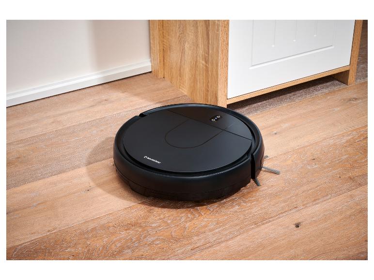 Aspirateur robot SilverCrest sur un parquet à côté d'une armoire blanche