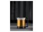 Mug en verre avec une anse noire, rempli de liquide ambré, sur fond sombre.