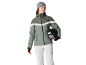 Femme avec bonnet gris, veste de ski verte et pantalon blanc, tenant un casque.