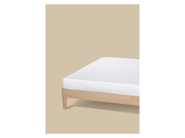 Matelas blanc sur un cadre de lit en bois clair sur fond beige.