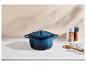 Cocotte en fonte bleue avec couvercle, cuillères en bois et moulins à sel et poivre sur un comptoir.