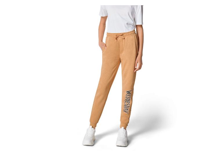 Pantalon de jogging beige avec le logo 'Wednesday' et des baskets blanches.