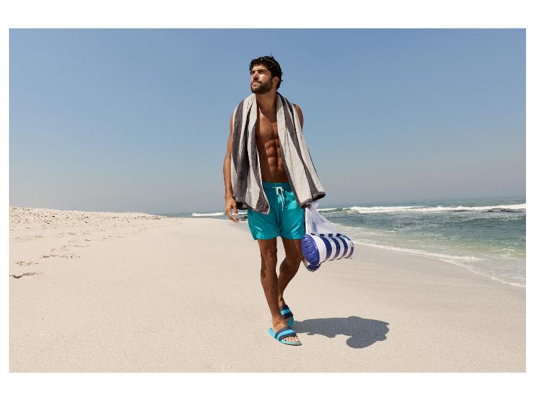 Homme en short de bain et serviette marchant sur la plage.