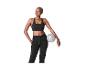 Femme souriante en brassière de sport noire et pantalon de survêtement, tenant un ballon de pilates gris.