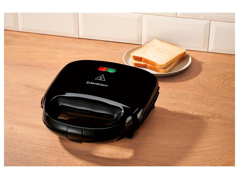 Appareil à croque-monsieur noir avec deux tranches de pain sur une assiette sur une surface en bois.