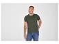 Homme en t-shirt vert foncé et jean bleu, souriant devant un mur blanc.