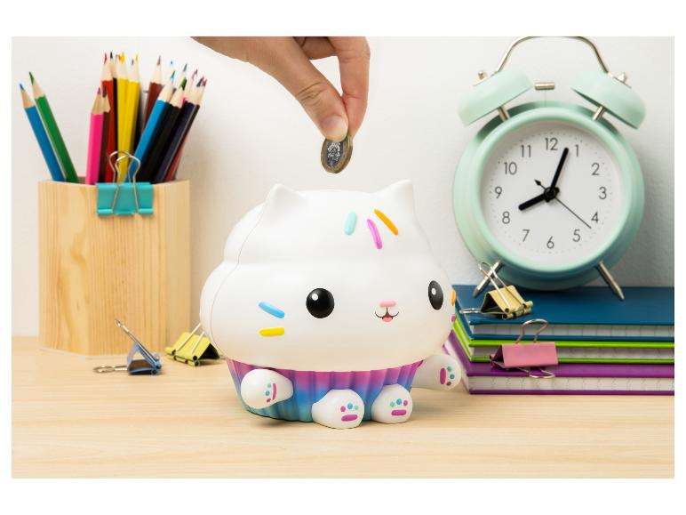 Main plaçant une pièce dans une tirelire chat-cupcake, avec des fournitures scolaires autour.