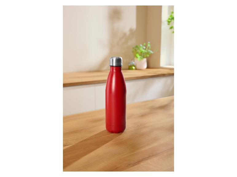 Bouteille d'eau isotherme rouge sur un comptoir de cuisine en bois avec des plantes en arrière-plan.