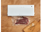 Machine sous vide avec bœuf scellé, ail et thym sur une planche à découper en bois.