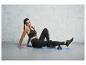 Une femme en tenue de sport fait des exercices avec un rouleau en mousse sur un tapis de yoga.
