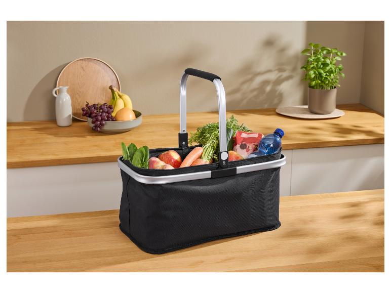 Panier de courses noir avec des produits d'épicerie, y compris des fruits, des légumes et de l'eau, sur un comptoir de cuisine.