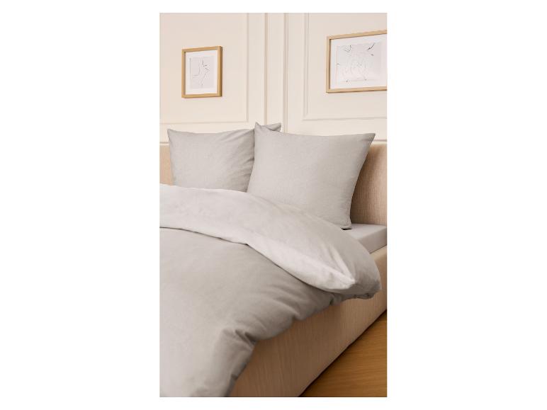 Drap-housse en jersey microfibre LIVARNO home sur un lit avec parure de lit grise.