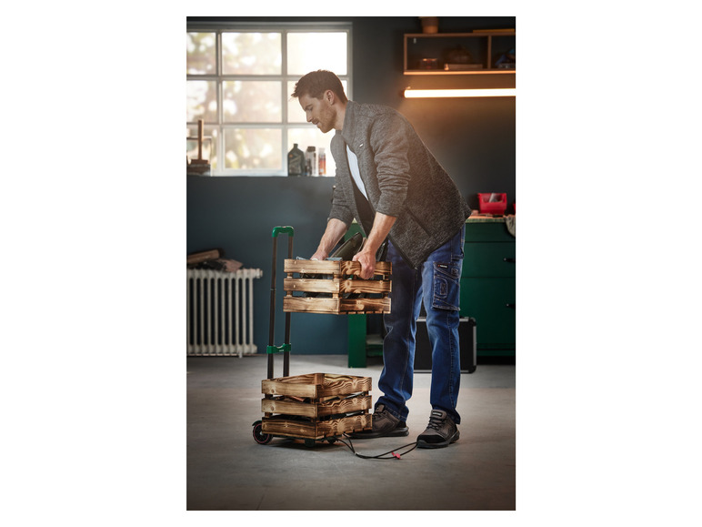 Un homme avec des chaussures de travail et des vêtements de travail place des caisses en bois sur un chariot.