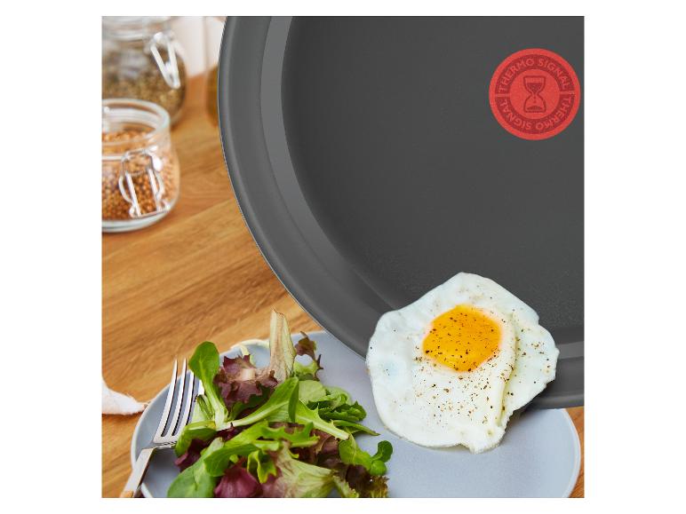 Poêle Tefal avec un œuf au plat et de la salade sur une assiette, épices en arrière-plan.