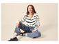 Femme souriante en pull rayé, jean et mocassins, assise sur le sol.