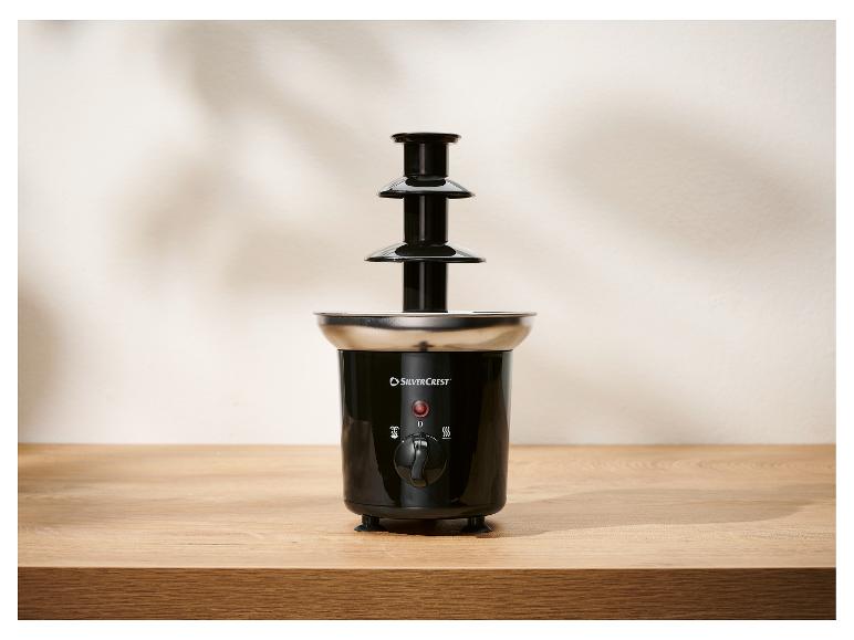 Une fontaine à chocolat noire à trois niveaux avec une base en acier inoxydable, sur une table en bois.