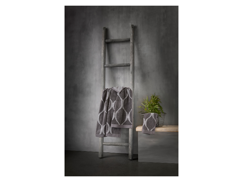Serviettes de bain grises à motifs accrochées à une échelle en bois contre un mur gris.