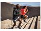 Deux personnes en tenue de sport montent des escaliers extérieurs, avec des montagnes en arrière-plan.