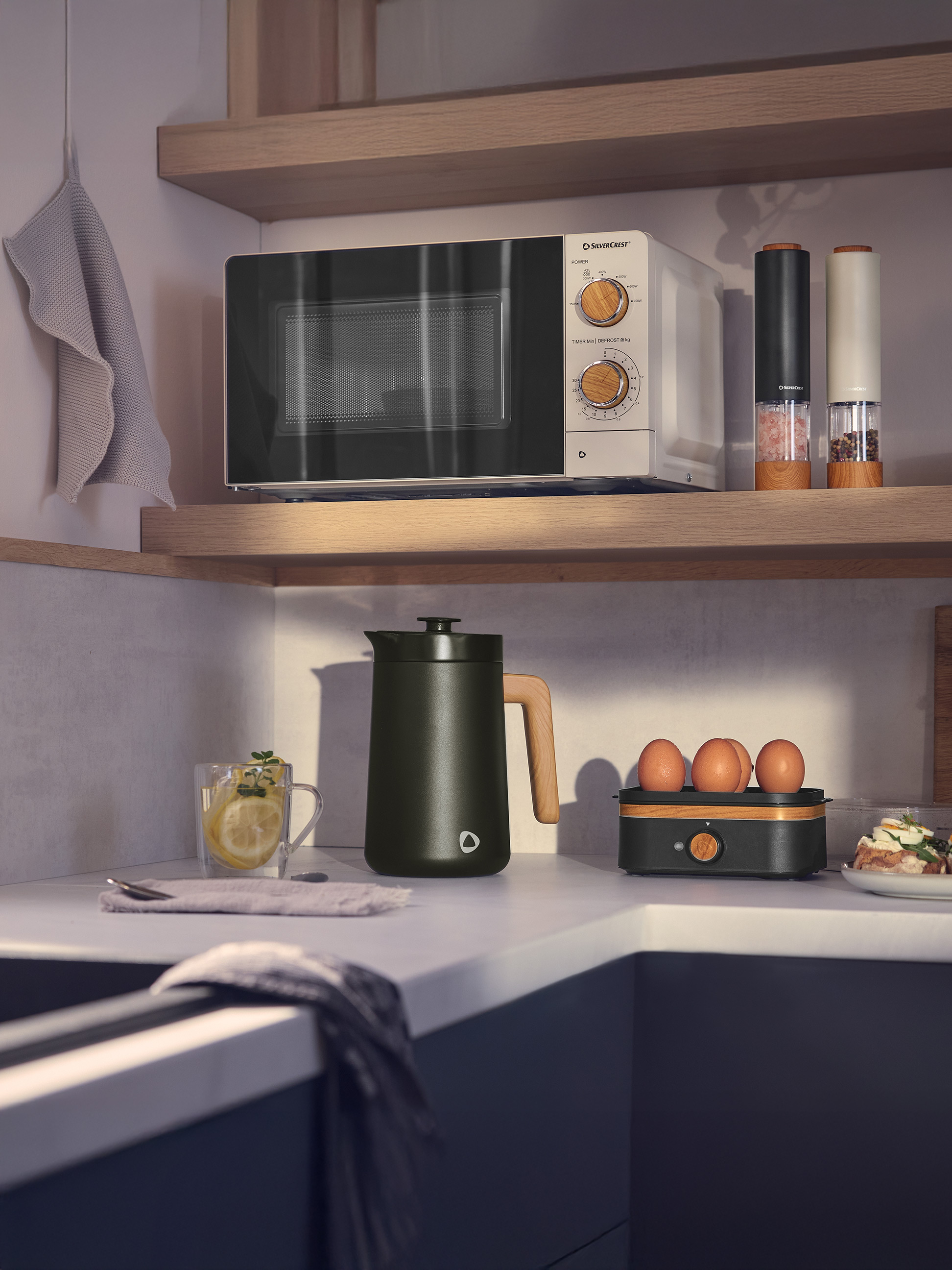 Micro-ondes blanc et noir avec détails en bois, bouilloire vert foncé et ustensiles de cuisine dans une cuisine moderne.