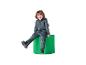 Enfant souriant en survêtement gris à capuche et chaussures noires, assis sur un cylindre vert.