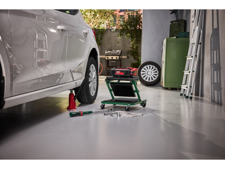 Voiture sur cric avec outils, chargeur et chariot roulant dans un garage.