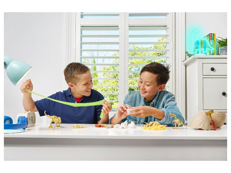 Deux garçons jouent avec des jouets dinosaures et de la pâte gluante à table.