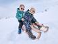 Des enfants en manteaux d'hiver et en bottes sur une luge dans la neige.