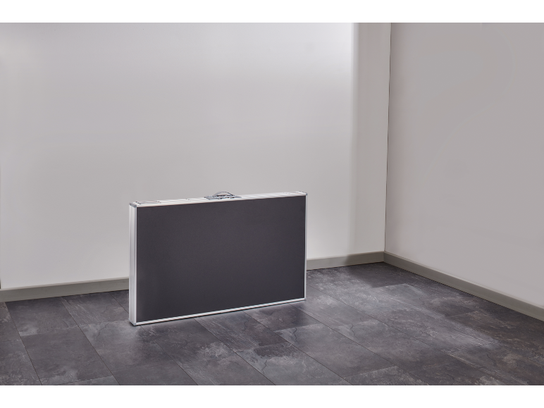 Une table pliante gris foncé dans un étui se trouve dans un coin d'une pièce avec un sol gris.